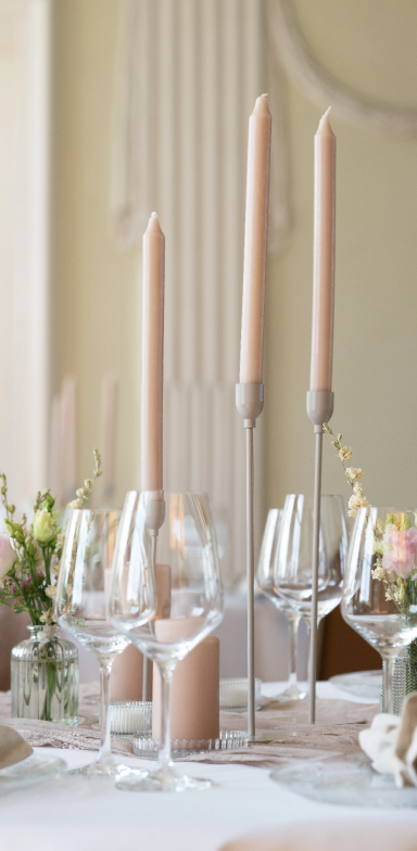 Elegant gedeckter Tisch mit Kerzen, Kerzenhaltern und Vasen mit Blumenarrangements.