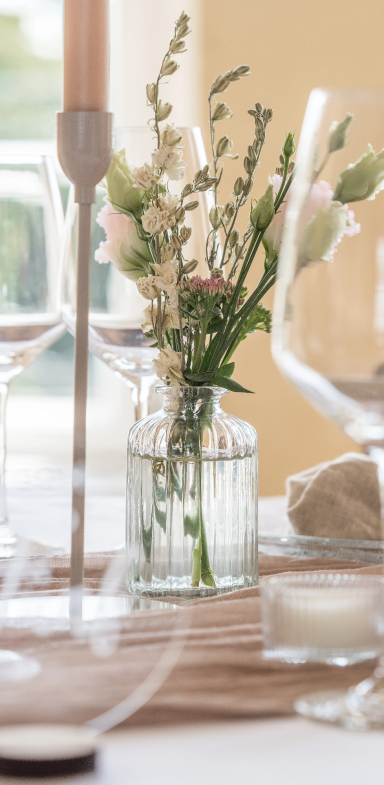 Ein Tischgedeck mit Kerzenhalter und einer Vase mit frischen Blumen.