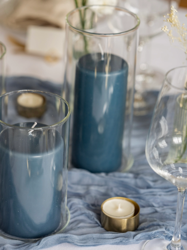 Zwei blaue Kerzen in gläsernen Haltern auf einem eleganten Tischgedeck.