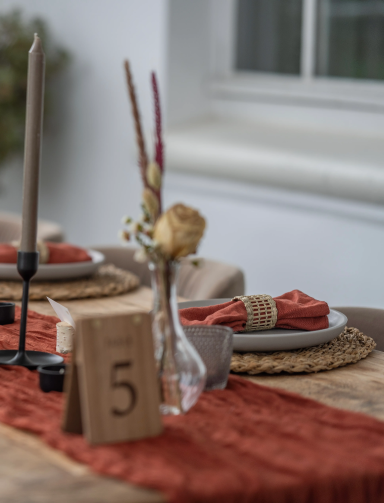 Tischdeko mit brauner Tischdecke, Kerzen, einer Blume und nummerierten Tischkarten.