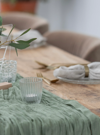 Ein gedeckter Tisch mit grüner Tischdecke, Gläsern und dekorativen Elementen.